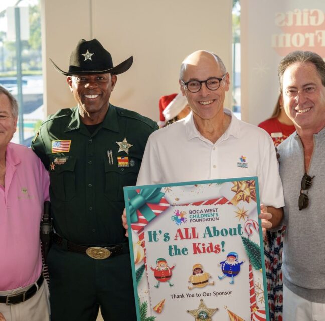 Four men with the It's All About The Kids sponsor sign, including a sheriff's deputy